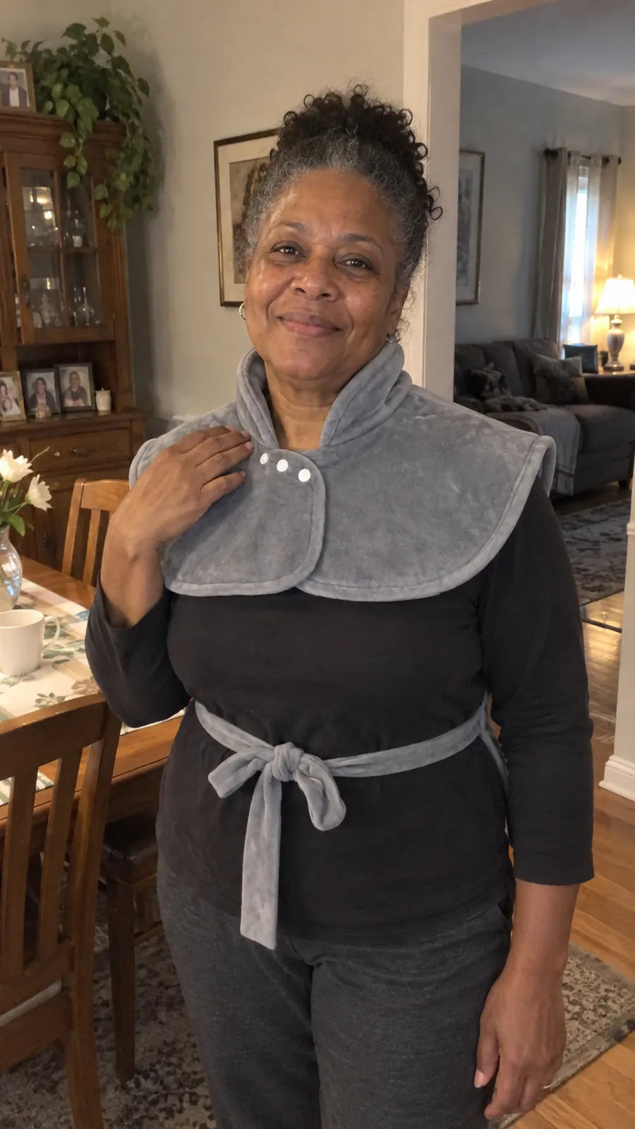 A smiling woman in her dining room wearing the Warmith wrap, collar snapped and waist tie knotted.