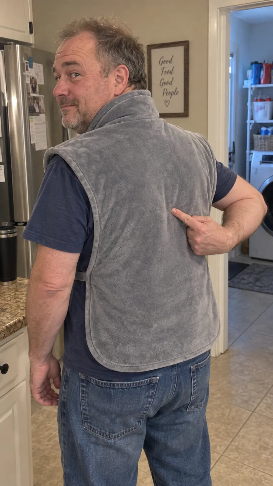 A man in his kitchen looking over his shoulder and pointing to his lower back, where the Warmith back panel reaches.