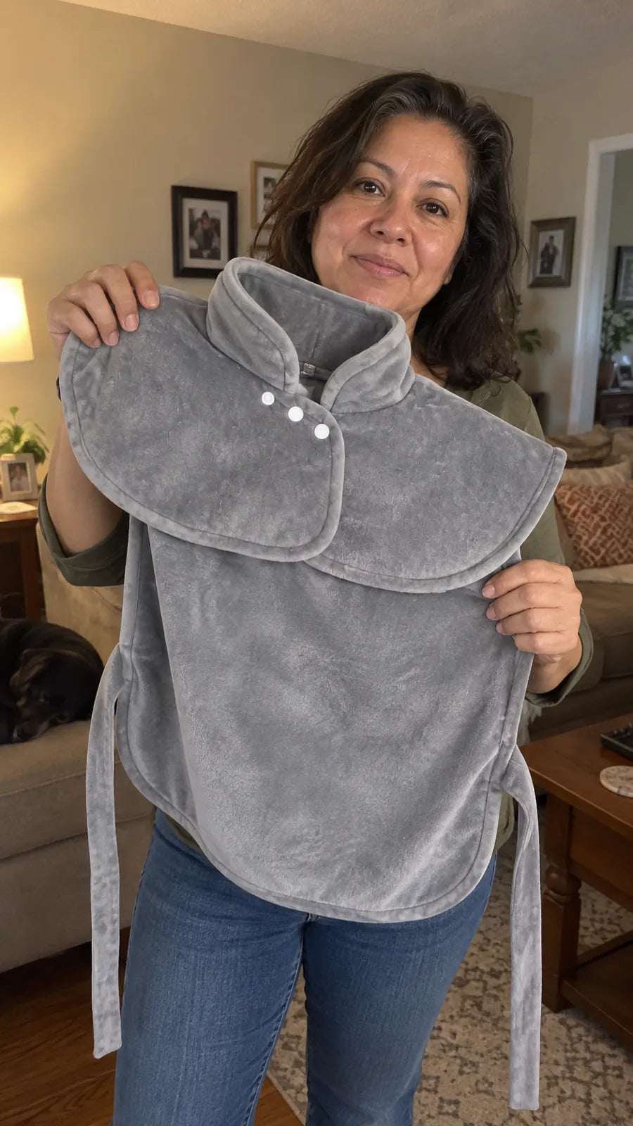 A woman in her living room holding up the Warmith wrap to show its collar, snaps, back panel and ties.