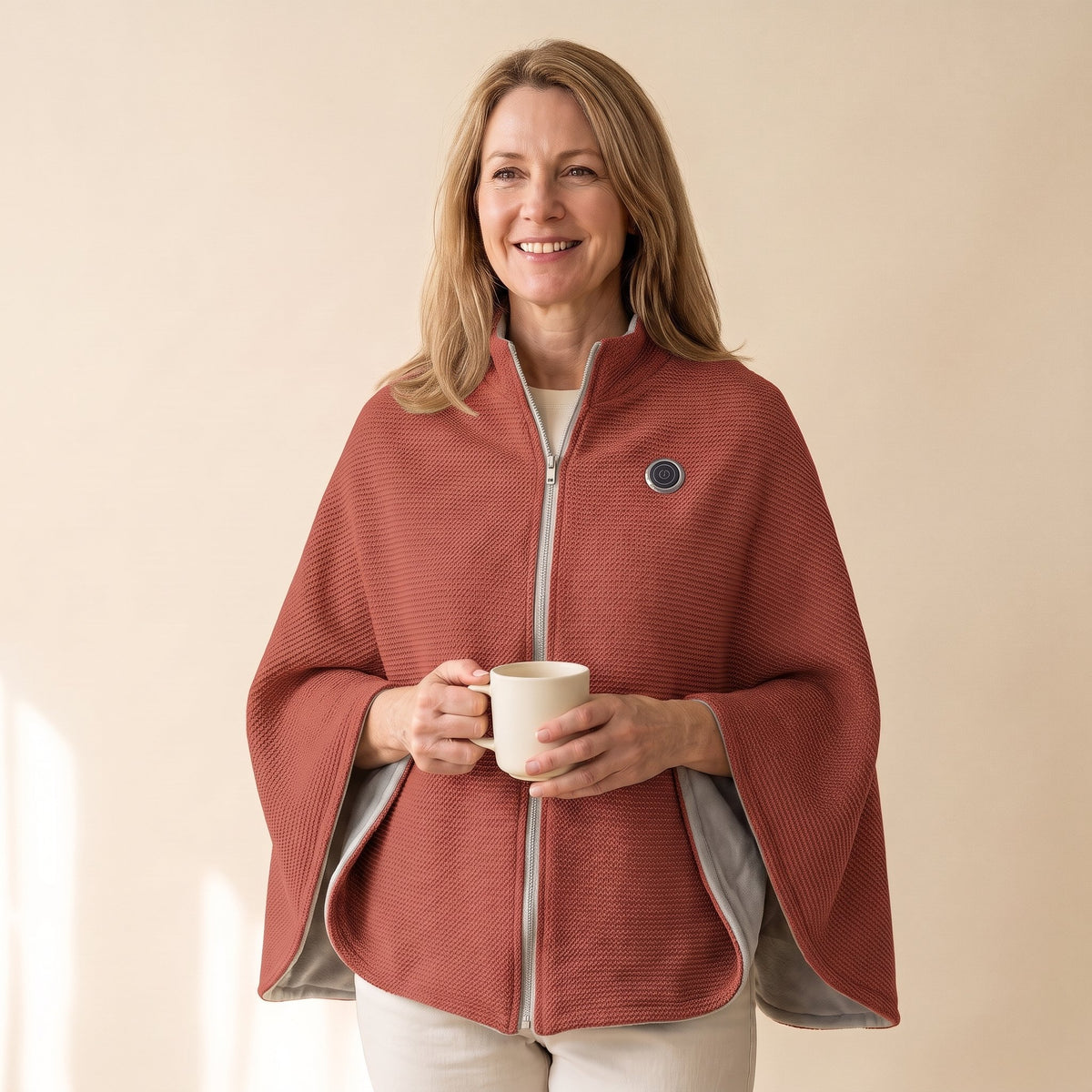 Woman wearing the brick red Warmith heated shawl wrap zipped, holding a mug