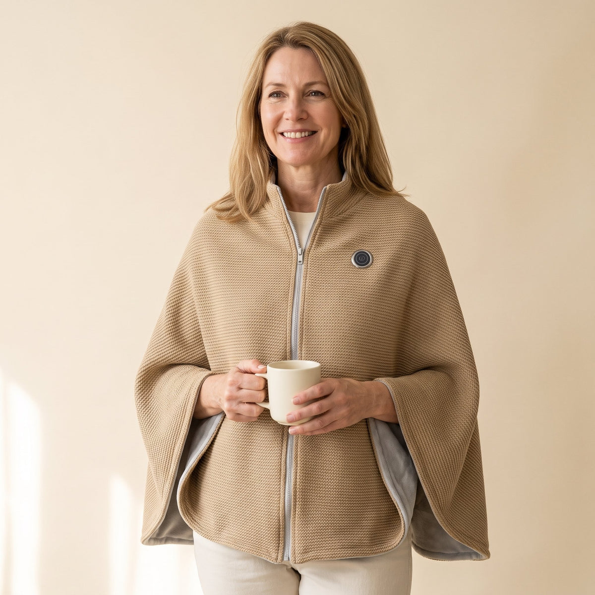 Woman wearing the camel Warmith heated shawl wrap zipped, holding a mug